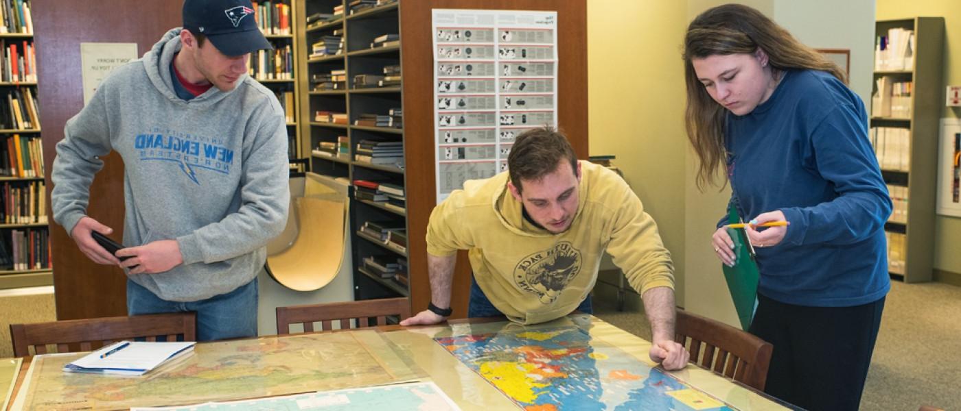 Three U N E 文科 students study a large map in the library